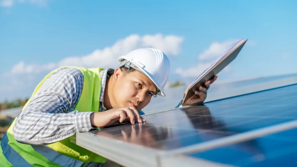 Técnico inspecionando painel solar fotovoltaico em telhado durante instalação ao ar livre.