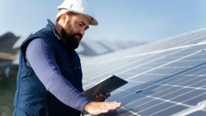 Profissional avaliando placas de energia solar em telhado utilizando tablet para monitoramento do sistema.